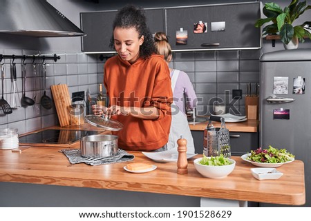 Waist up portrait of the multiracial calm woman preparing pasta for the dinner while cooking at the kitchen with her best friend. Coolinary concept. Stock photo