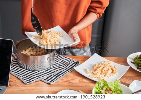 Happy multiracial woman cooking in her modern kitchen. Girl pouring pasta at the plate from the pan while cooking with her best friend. Coolinary concept. Stock photo