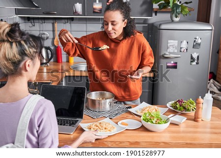Smells good. Attractive talented curly woman smells pasta while preparing dinner for herself and fir her best friend. Girls spending time at the kitchen. Stock photo