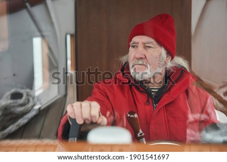 Navigation and control on a yacht. Confident mature sailor man standing at the steering wheel and panel of instruments while floating at the yacht in sea. Senior man looking at the window. Stock photo