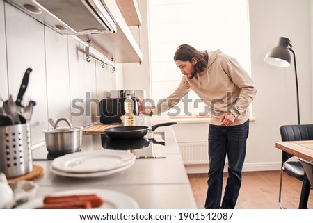 Handsome unshaven man wearing casual clothes preparing to making toasts while doing breakfast at the kitchen. Coolinary concept. Stock photo