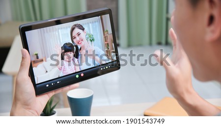 back view of asian young man has video chat with his wife and their daughter by digital tablet at home happily