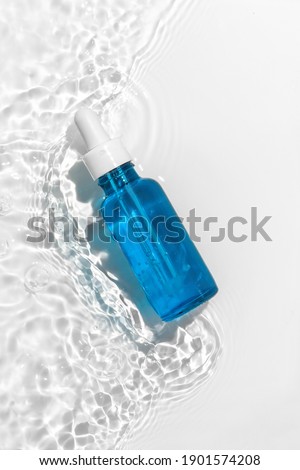 Blue cosmetic bottle on the water surface. Blank label for branding mock-up. Summer water pool fresh concept. Flat lay, top view.