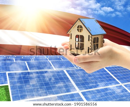 The photo with solar panels and a woman's palm holding a toy house shows the flag of Latvia in the sun.