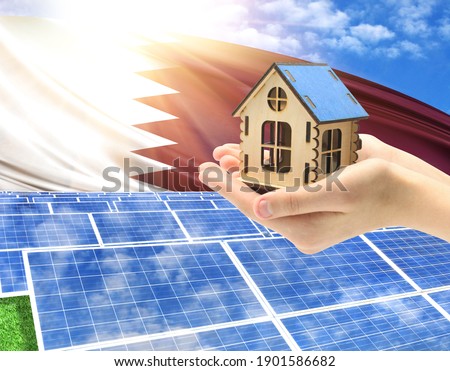 The photo with solar panels and a woman's palm holding a toy house shows the flag of Qatar in the sun.