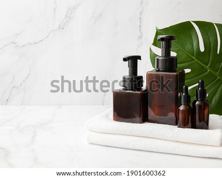 Amber glass cosmetic bottles set with towel and monstera leaf on marble background. Blank label for branding mock-up. Natural beauty product concept. Copy space