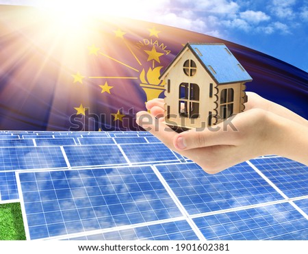 The photo with solar panels and a woman's palm holding a toy house shows the flag State of Indiana in the sun.