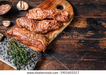 Raw Marinated skirt steaks in bbq sauce on a wooden cutting board with herbs. Dark wooden background. Top view. Copy space.