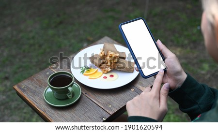 Young female using smart phone taking pictures of coffee and cake during resting in cafe.