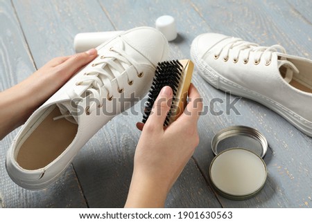 Woman cleaning stylish footwear on grey wooden background, closeup. Shoe care accessories Royalty-Free Stock Photo #1901630563