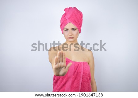 Young beautiful woman wearing shower towel after bath standing over isolated white background serious and doing stop sing with palm of the hand.