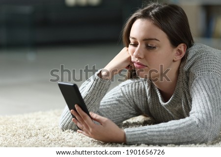 Bored teen checking smart phone lying on the floor at home Royalty-Free Stock Photo #1901656726