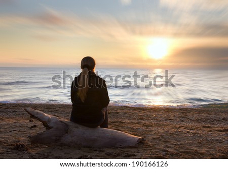 Female silhouette on seacoast against the sunset sky