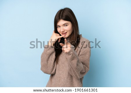 Young Ukrainian teenager girl wearing a sweater over isolated blue background making phone gesture and pointing front