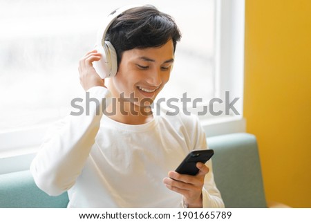 Asian man sitting, enjoying music Royalty-Free Stock Photo #1901665789