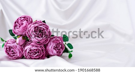 Bouquet of beautiful violet peonies on white silk fabric background. Copy space. Greeting card. Flowers for present