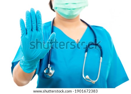 Female nurse with stethoscope puts rubber gloves and wearing medical face mask, woman doctor in blue uniform show hand up stop sign, studio shot isolated over white background, medical health concept