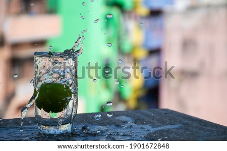 Raw lemon falling down in transparent glass filled with water with big splashes against blur background.