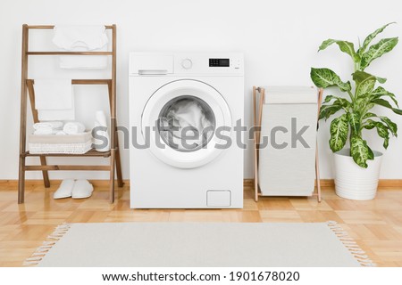 Interior of laundry room with modern washing machine and textile Royalty-Free Stock Photo #1901678020