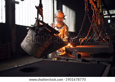 Workman in protective suit hardworking with liquid metal in foundry. Royalty-Free Stock Photo #1901678770