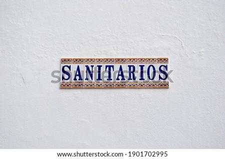 Close Up of Decorative Ceramic Tile Sign 'Sanitarios' on White Wall Translates as 'Toilets' 