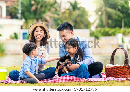 An Asian family plays with a Shiba Inu dog. Happy family with pet dog at picnic in a sunny day. Royalty-Free Stock Photo #1901712796