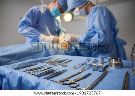 Plastic surgery instruments on surgical table with medical team and patient on blurred background. Doctor and assistant performing aesthetic surgery. Concept of plastic surgery and medical instruments Royalty-Free Stock Photo #1901723767