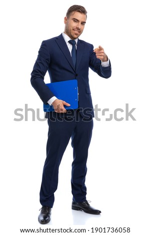 full body picture of elegant man in navy blue suit holding clipboard and pointing finger on white background, smiling and standing isolated in studio