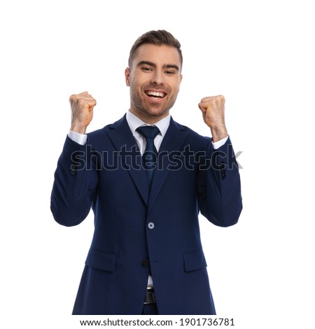 proud elegant man in navy blue suit holding fists in the air and celebrating victory, laughing and having fun, standing isolated on white background in studio, portrait