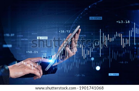 Hand of businesswoman using tablet computer in blurry office with double exposure of financial charts. Toned image