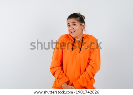  female in orange hoodie looking at camera and looking confused , front view. 