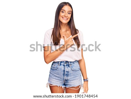Young hispanic woman wearing casual white tshirt cheerful with a smile on face pointing with hand and finger up to the side with happy and natural expression 