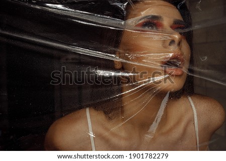 Photo portrait of brunette woman wearing make-up breathing behind transparent cellophane covered with water drops