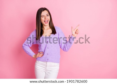 Photo of optimistic girl point empty space blink wear lilac sweater trousers isolated on pink color background