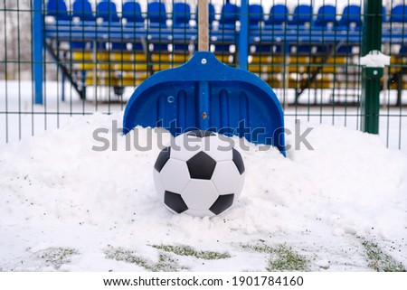 Classic soccer ball, snow-covered football field and shovel on winter stadium outdoor