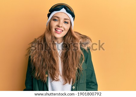 Beautiful blonde caucasian woman wearing snow wear and sky glasses looking positive and happy standing and smiling with a confident smile showing teeth 