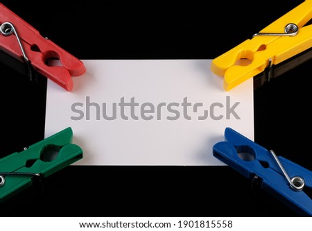 White sheet of note paper on black background with clothespins close-up macro photography