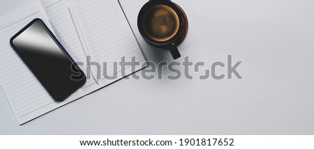Top view of mock up smart phone, empty notebook, coffee cup and copy space on white table. 