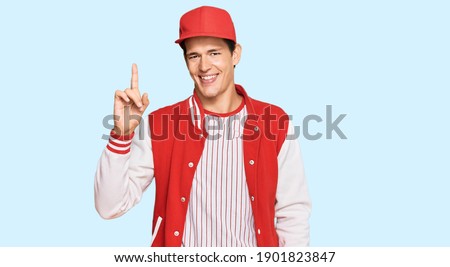 Handsome caucasian man wearing baseball uniform showing and pointing up with finger number one while smiling confident and happy. 