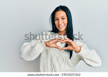 Beautiful hispanic woman wearing casual winter sweater over white background smiling in love doing heart symbol shape with hands. romantic concept. 