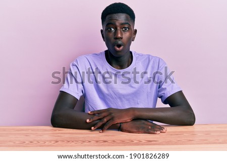 Young african american man wearing casual clothes sitting on the table scared and amazed with open mouth for surprise, disbelief face 