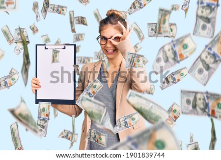 Beautiful caucasian woman with blonde hair holding clipboard with blank space smiling happy doing ok sign with hand on eye looking through fingers