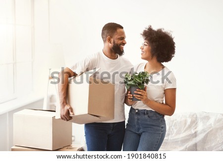Cheerful Black Couple Carrying Packed Boxes Moving To New Apartment Standing Indoors. Own House And Real Estate, Young Family Housing. Love Nest Concept