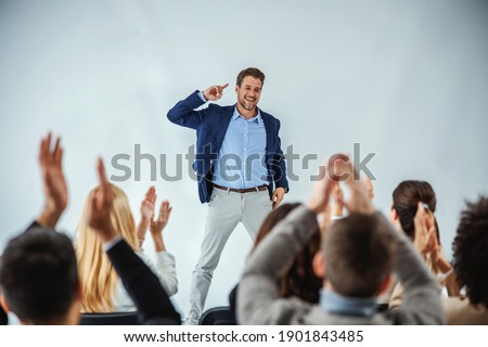 Smiling motivational speaker standing in front of his audience who is clapping. Royalty-Free Stock Photo #1901843485