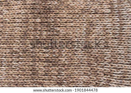 Knitted background. Knitted wallpaper. Beige knitted fabric. Knitted texture. Soft material. Brown, beige and white handmade sweater close up photo. Cozy background. Knitwear detail. Woolen cloth. Royalty-Free Stock Photo #1901844478