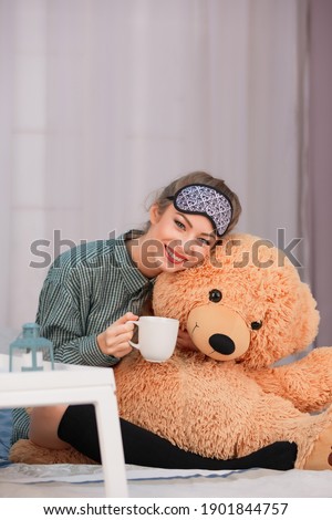 Breakfast in bed. Young woman smiles, drinks coffee tea and hugs big toy bear. High quality photo