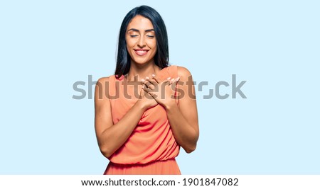 Beautiful hispanic woman wearing summer dress smiling with hands on chest with closed eyes and grateful gesture on face. health concept. 