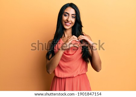 Beautiful hispanic woman wearing summer dress smiling in love showing heart symbol and shape with hands. romantic concept. 