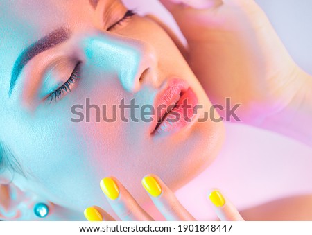 High Fashion model girl in colorful bright UV lights posing in studio, portrait of beautiful woman with trendy make-up and manicure. Art design, colorful make up. Over colourful background