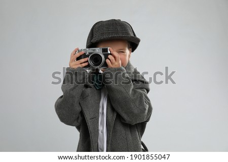 Cute little detective taking photo with vintage camera on grey background